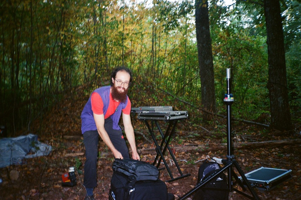 David Richard setting up a keyboard rig and mic stand at an outdoor set in the woods